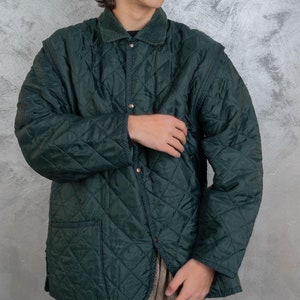 Peut inclure: Une veste matelassée vert foncé avec un col en velours côtelé et une fermeture à pression. La veste a un motif en losange et une poche plaquée sur le côté gauche.