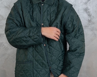 Puede incluir: Una chaqueta acolchada de color verde oscuro con cuello de pana y cierre de presión. La chaqueta tiene un patrón de rombos y un bolsillo de parche en el lado izquierdo.