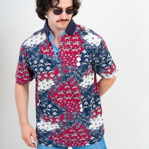 Peut inclure: Un polo à manches courtes arborant un motif multicolore de chevaux et de cavaliers dans des tons rouge, bleu marine et blanc. Le vêtement présente un col bleu marine foncé, une patte de boutonnage bleu clair et un jean bleu clair.
