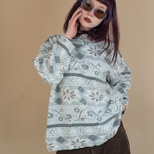 Puede incluir: Una mujer con un suéter estampado en gris y blanco, una falda de pana marrón y gafas de sol ovaladas azules.