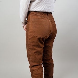 May include: Brown suede trousers with a high waist and a straight leg. The trousers are made from a soft, supple material and have a classic look.