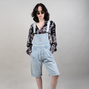 May include: A person wearing light blue denim overalls with a black and white patterned shirt, sunglasses, and white sneakers with black stripes.