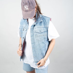 Könnte beinhalten: Eine hellblaue Jeansweste mit einem weißen T-Shirt und Jeans-Shorts. Die Weste hat einen Knopfverschluss und zwei Taschen. Die Person trägt eine graue Baseballkappe mit den Buchstaben "NY" auf der Vorderseite.