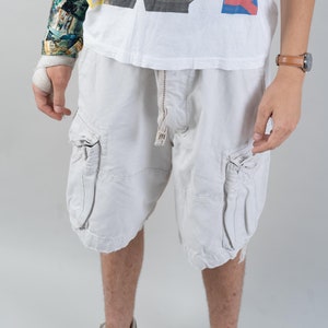 Könnte beinhalten: Ein weißes T-Shirt mit einem Schwarzweißbild einer Person, die Gitarre spielt. Auf dem T-Shirt steht in roten und blauen Buchstaben "ARVEY". Die Person trägt einen schwarzen Anzug und ein weißes Hemd. Die Person hält eine schwarze E-Gitarre. Die Person trägt eine braune Lederuhr am linken Handgelenk. Die Person trägt eine weiße Cargohose. Die Person hat einen Verband am linken Handgelenk.