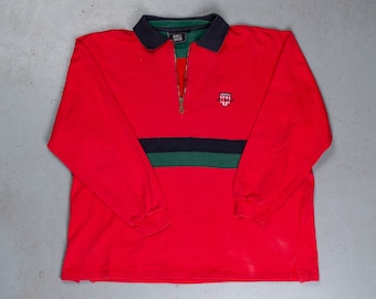 May include: Red long-sleeved polo shirt with a black zip, black and green stripes, and a small embroidered logo on the chest.