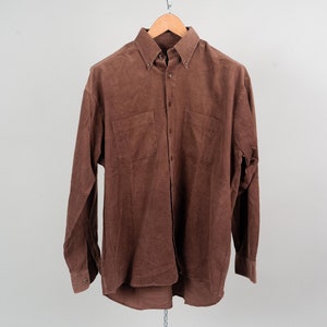 Può includere: Una camicia a maniche lunghe in velluto a coste marrone con colletto abbottonato e due tasche sul petto.