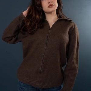 Peut inclure: Une femme portant un pull marron zippé et un jean bleu. Elle regarde vers le haut et vers la droite.