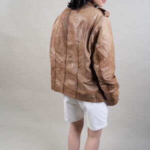 May include: A brown leather jacket with a white t-shirt underneath. The person is wearing white shorts and white trainers with black accents.