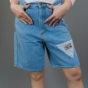Könnte beinhalten: Hellblaue Jeans-Shorts mit einem gestreiften Dreiecks-Patch am rechten Bein. Der Patch zeigt eine Comicfigur mit dem Wort "Free" darauf.