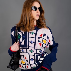 Könnte beinhalten: Eine Frau trägt einen pinkfarbenen, blauen, roten und grünen geometrischen Pullover mit einem schwarzen Lederrock und einer schwarzen Sonnenbrille.