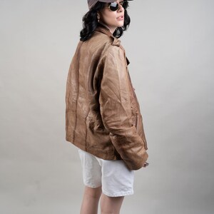 May include: A woman wearing a brown leather jacket, white shorts, and a black baseball cap with the letters "NY" on it. She is also wearing sunglasses.