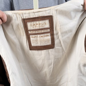 May include: A brown leather label with the text "CAMPUS by Marc O'Polo" and "Registered Trademark since 1972". Below the text is a smaller label with the text "PULP DELUXE NETWORK STRONGLY RECOMMENDS" and a paragraph of text in German.