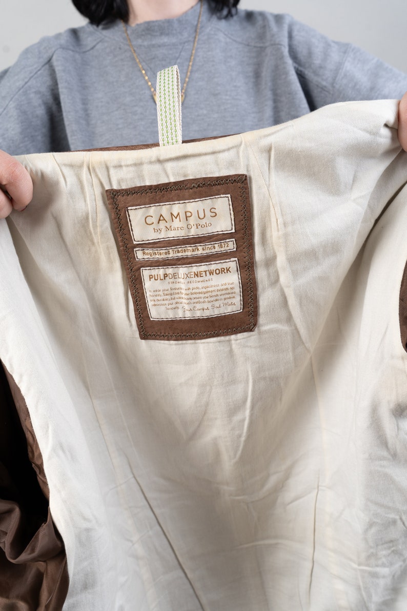 May include: A brown leather label with the text "CAMPUS by Marc O'Polo" and "Registered Trademark since 1972". Below the text is a smaller label with the text "PULP DELUXE NETWORK STRONGLY RECOMMENDS" and a paragraph of text in German.