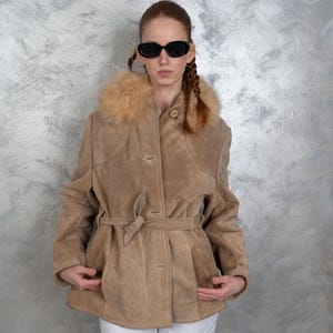 Könnte beinhalten: Eine braune Wildlederjacke mit einem Kunstfellkragen und einem Gürtel. Die Jacke hat einen Knopfverschluss und zwei Taschen.