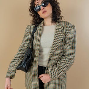 May include: A brown, black, and white plaid blazer with a black leather shoulder bag. The blazer has a button closure and a notched collar.