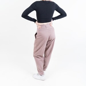 Könnte beinhalten: Eine Person trägt ein schwarzes, langärmliges Crop-Top und eine braune, hochgeschlossene Hose. Sie trägt weiße Turnschuhe und hat ihre Haare zu einem Pferdeschwanz gebunden.