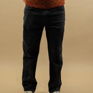May include: A pair of dark blue corduroy pants with a straight leg fit. The pants are worn by a person standing with their hands in their pockets.