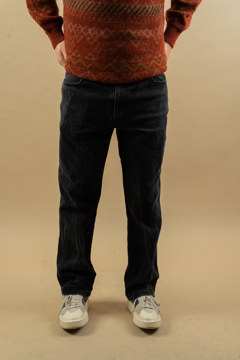 May include: A pair of dark blue corduroy pants with a straight leg fit. The pants are worn by a person standing with their hands in their pockets.