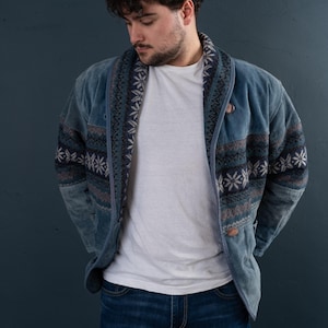 Può includere: Una giacca di jeans blu con un design a motivi in ​​tinte di blu, bianco e grigio. La giacca ha un colletto e una chiusura con bottoni.