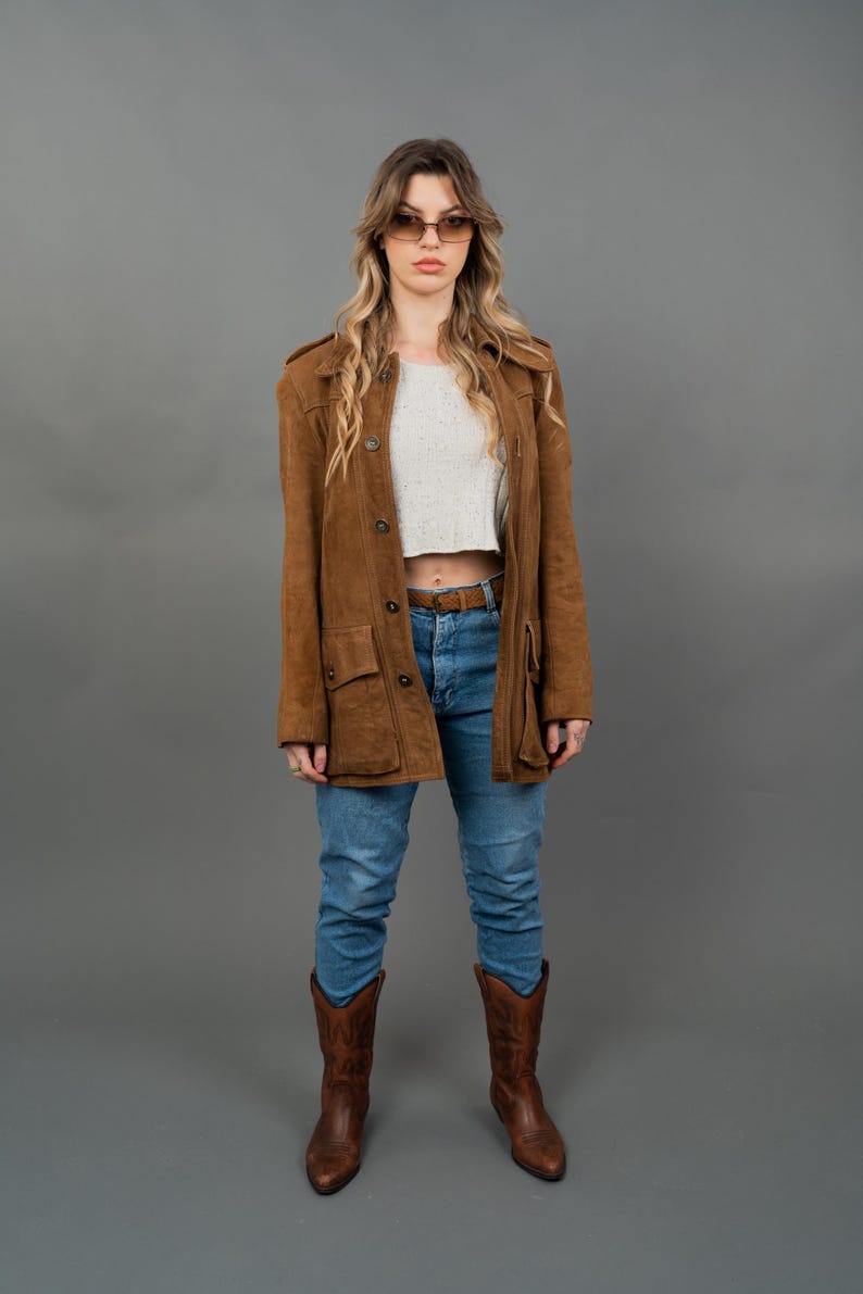 Peut inclure: Veste en daim marron &agrave; boutons, port&eacute;e sur un crop top blanc et un jean bleu. La tenue est compl&eacute;t&eacute;e par des bottes de cowboy marron. La veste a des poches et un col.