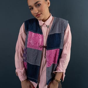 Könnte beinhalten: Eine Patchwork-Jeansweste mit rosa und blauen Stoffbahnen. Die Weste hat einen Bindeverschluss vorne und ein rosafarbenes Schlangenhautmuster auf zwei der Bahnen.