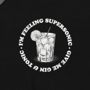 以下が含まれることがあります： 白い円形のグラフィックが施された黒いスウェットシャツ。グラフィックには、ジンとトニックの飲み物と「Give me gin & tonic - I'm feeling supersonic.」というテキストが描かれています。