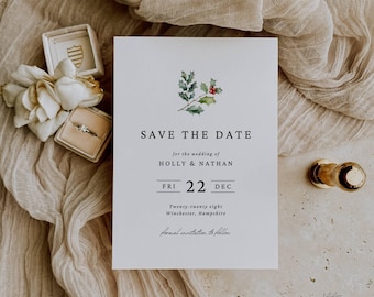 May include: A white wedding invitation with the text "SAVE THE DATE" and the names "HOLLY & NATHAN". The date is December 22. The invitation features a watercolor holly and berry design. A ring box and gold accents are visible.