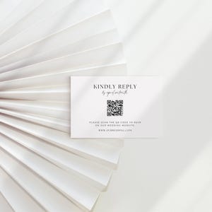 May include: A white RSVP card with black text that reads "KINDLY REPLY" and "by april sixteenth." A QR code is below the text, with the prompt "PLEASE SCAN THE QR CODE TO RSVP ON OUR WEDDING WEBSITE: www.OURWEDDING.COM."