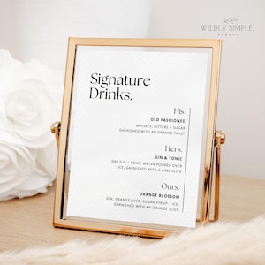 May include: A gold-framed sign with a white background and black text. The sign lists signature drinks with names and ingredients: Old Fashioned, Gin & Tonic, and Orange Blossom.