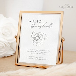 May include: A gold-framed sign with the words "AUDIO Guestbook" in elegant script. Below, a line drawing of a vintage telephone. The text reads, "The newlyweds can't come to the phone right now. Please leave a message..."