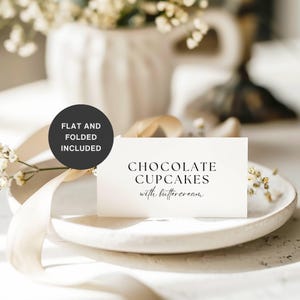 Puede incluir: Una tarjeta blanca sobre un plato blanco con el texto "CHOCOLATE CUPCAKES with buttercream". Un círculo negro con el texto "FLAT AND FOLDED INCLUDED" está en la parte superior izquierda. Un jarrón blanco con flores en el fondo.