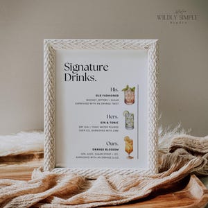 Op de afbeelding: Een wit ingelijst bord met de titel "Signature Drinks" en drie drankrecepten: "His. Old Fashioned", "Hers. Gin & Tonic" en "Ours. Orange Blossom". Elk recept bevat een lijst met ingrediënten en een kleine aquarelillustratie van een cocktail.