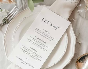 May include: A wedding menu card with the words "LET'S eat" in elegant script. The menu lists a starter, main course, and dessert. The card is on a white plate with a silver rim, next to a fork and spoon.