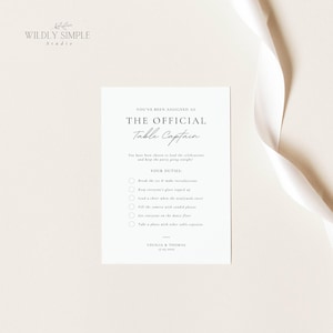 Könnte beinhalten: Eine weiße, rechteckige Hochzeitstischkarte mit schwarzem Text, der YOU'VE BEEN ASSIGNED AS THE OFFICIAL Table Captain lautet. Sie listet Aufgaben wie Eisbrechen, Gläser füllen und Fotos machen auf, signiert von Cecilia & Thomas.