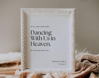 May include: A white framed sign with the text "Dancing With Us in Heaven." The sign includes the names "Emma & Noah" and the date "17.05.2X." The frame has a textured, carved design. The sign is on a wooden tray with a beige cloth.