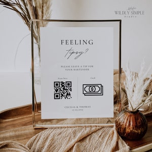 May include: A white sign with black text and graphics in a gold frame. The sign reads "Feeling Tipsy? Please leave a tip for your bartender." It includes a QR code and a cash icon. The sign also includes the names "Cecilia & Thomas" and the date "17.05.2025".