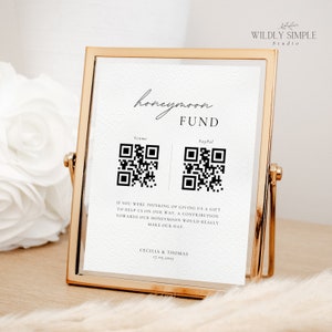 May include: A white card with black text in a gold frame. The card says "honeymoon fund" and has QR codes for Venmo and PayPal. The text below the QR codes says "If you were thinking of giving us a gift to help us on our way, a contribution towards our honeymoon would really make our day." The card is signed "Cecilia & Thomas 17.05.2025".