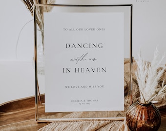 May include: A white sign in a gold frame with the text "To all our loved ones, Dancing with us in Heaven, We love and miss you, Cecilia & Thomas, 17.05.2015". The sign is sitting on a table with a vase of dried flowers.