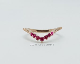 May include: A delicate gold ring with a V-shaped design featuring a row of small red gemstones. The ring is set with a row of smaller gemstones along the band.