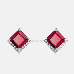 May include: A pair of silver earrings with a square red gemstone surrounded by a halo of smaller white gemstones.