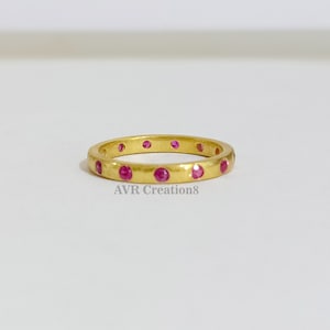 May include: A gold band ring with a hammered texture and small pink gemstones set around the band. The text "AVR Creation8" is visible below the ring.