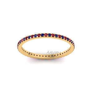 May include: A gold-colored ring with a band of alternating red and blue gemstones. The ring is set against a white background. The brand name "AAVIRA" is printed on the ring.