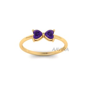 May include: A gold ring with two heart-shaped amethyst gemstones. The gemstones are set in a bow shape.