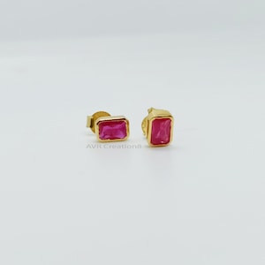 May include: A pair of gold stud earrings featuring rectangular, bright pink gemstones. The earrings are set in a gold bezel setting. The earrings are displayed on a white background. The text "AVR Creation8" is visible.