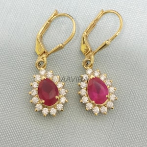 May include: A pair of gold earrings with a teardrop-shaped red gemstone surrounded by a halo of smaller white gemstones.