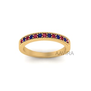 May include: A gold band ring with a row of red and blue gemstones. The ring has a rope-like design around the band.