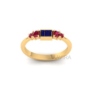 May include: A gold band ring with a rectangular blue gemstone and smaller red gemstones on either side.