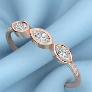 Op de afbeelding: Ros&eacute;gouden ring met drie marquise-geslepen diamanten en kleine accentstenen. De ring heeft een delicate band en een gepolijste afwerking, tegen een lichtblauwe achtergrond. Een sieraad voor dagelijks gebruik of speciale gelegenheden.