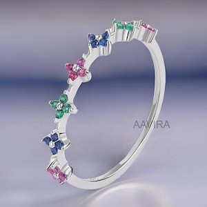 May include: A silver ring with five small flower-shaped settings, each with a different colored gemstone. The gemstones are pink, blue, green, and a darker blue.