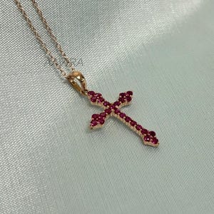 May include: A rose gold necklace with a cross pendant encrusted with small red gemstones.